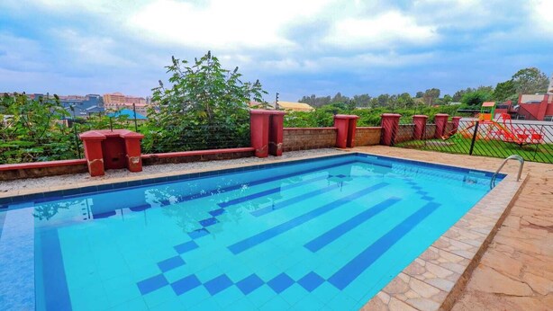 Une piscine rectangulaire aux carreaux bleus, bordée de pierres, entourée d’un petit muret en pierre et de jardinières rouges.