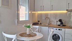 Una cocina moderna con armarios blancos, lavadora integrada y un comedor con una mesa redonda y dos sillas.