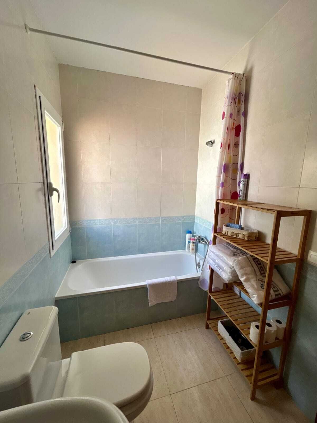 Une salle de bain équipée d’une baignoire, de toilettes et d’une étagère où sont rangés les articles de toilette.