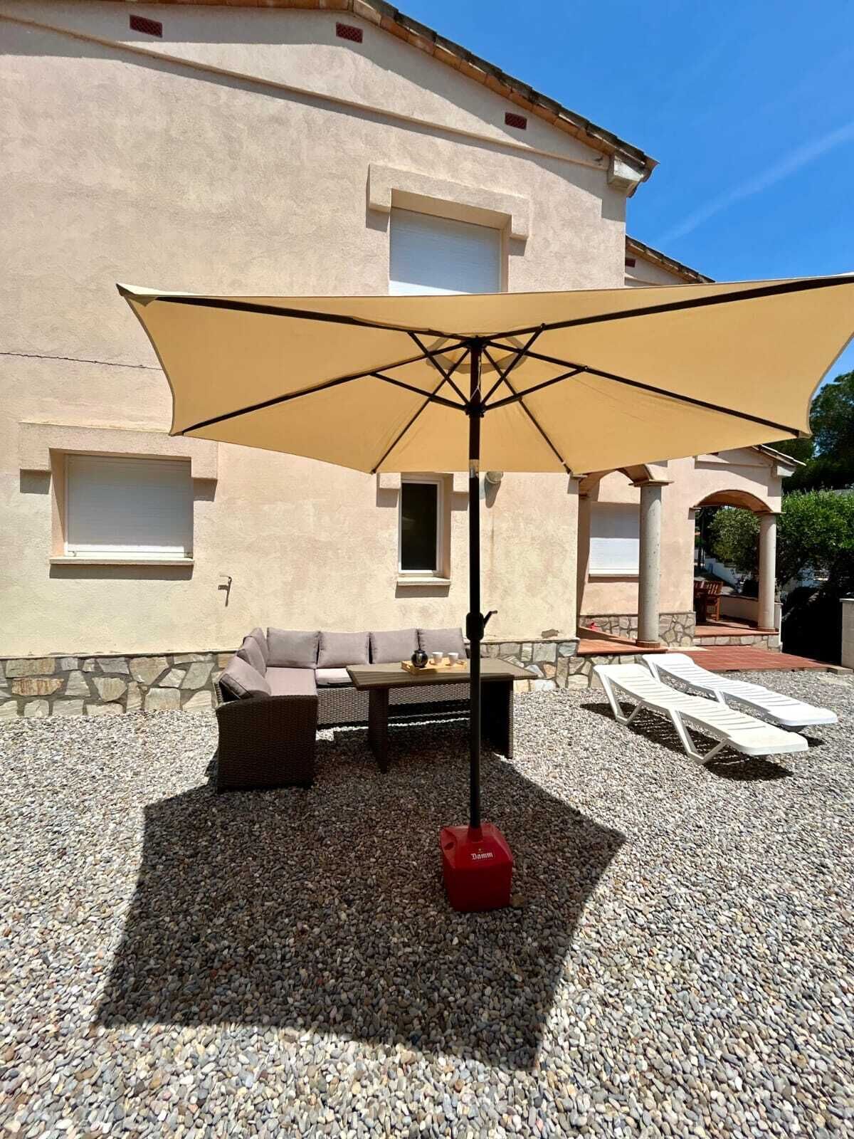 An outdoor seating area with a table and chairs, a large umbrella, and a red object on the ground.