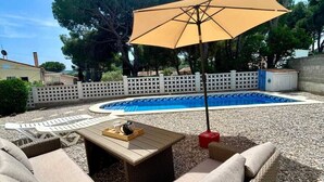 A poolside area with wicker furniture, a table with a tray, and a large umbrella. - Villa Rosell (L'Escala)