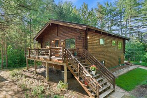 Una cabaña de madera con terraza y escaleras, rodeada de árboles.