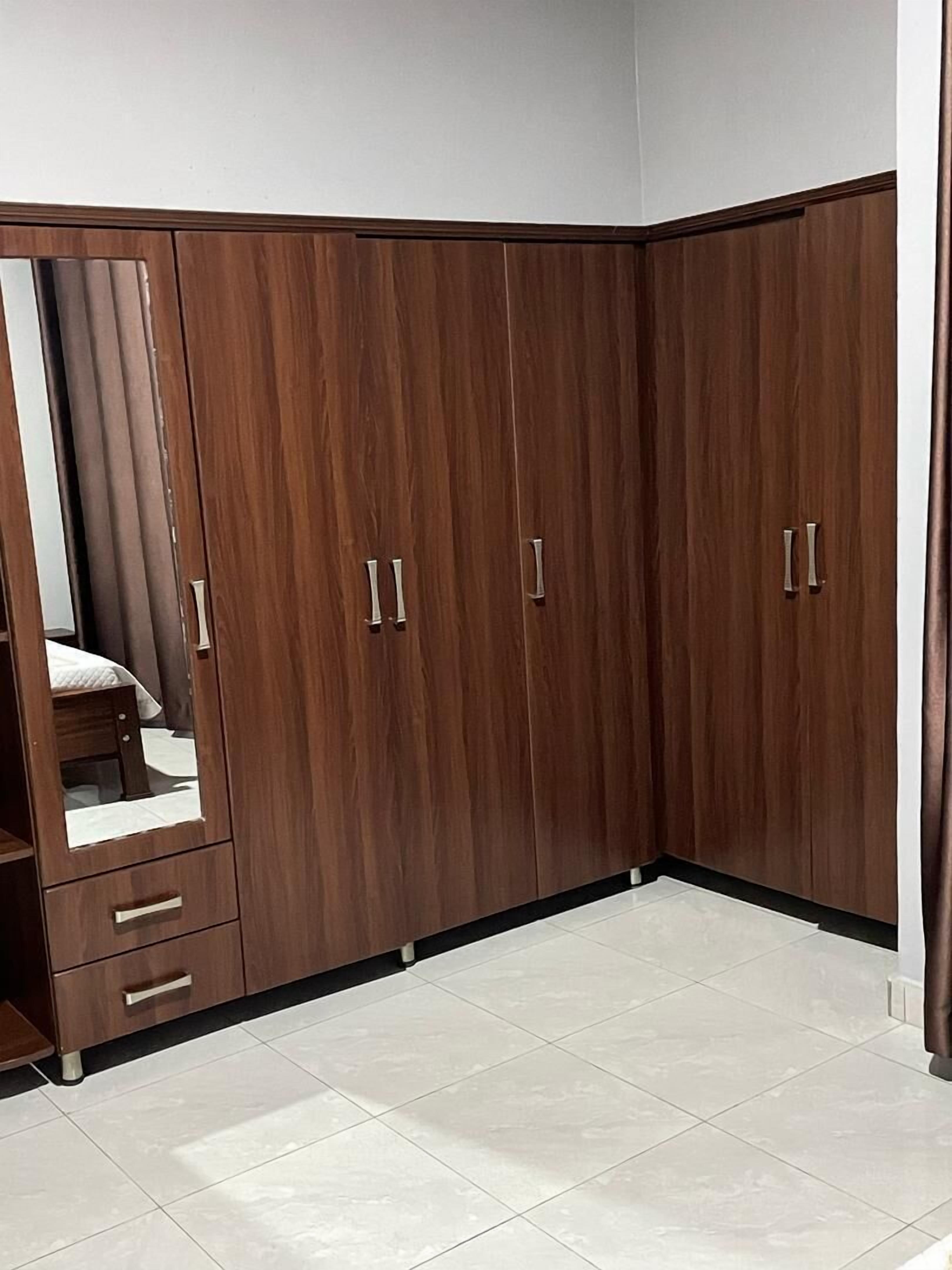 A corner room with a large wardrobe, a mirror, and a small bed.