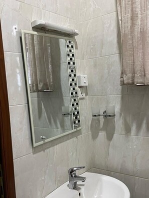 Ein Badezimmer mit weißem Waschbecken, einem Spiegel, einem Handtuchhalter und einer Seifenspender.