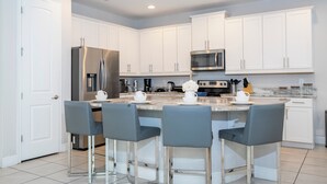 Een moderne keuken met witte kasten, roestvrijstalen apparatuur en een centraal eiland met barstoelen.