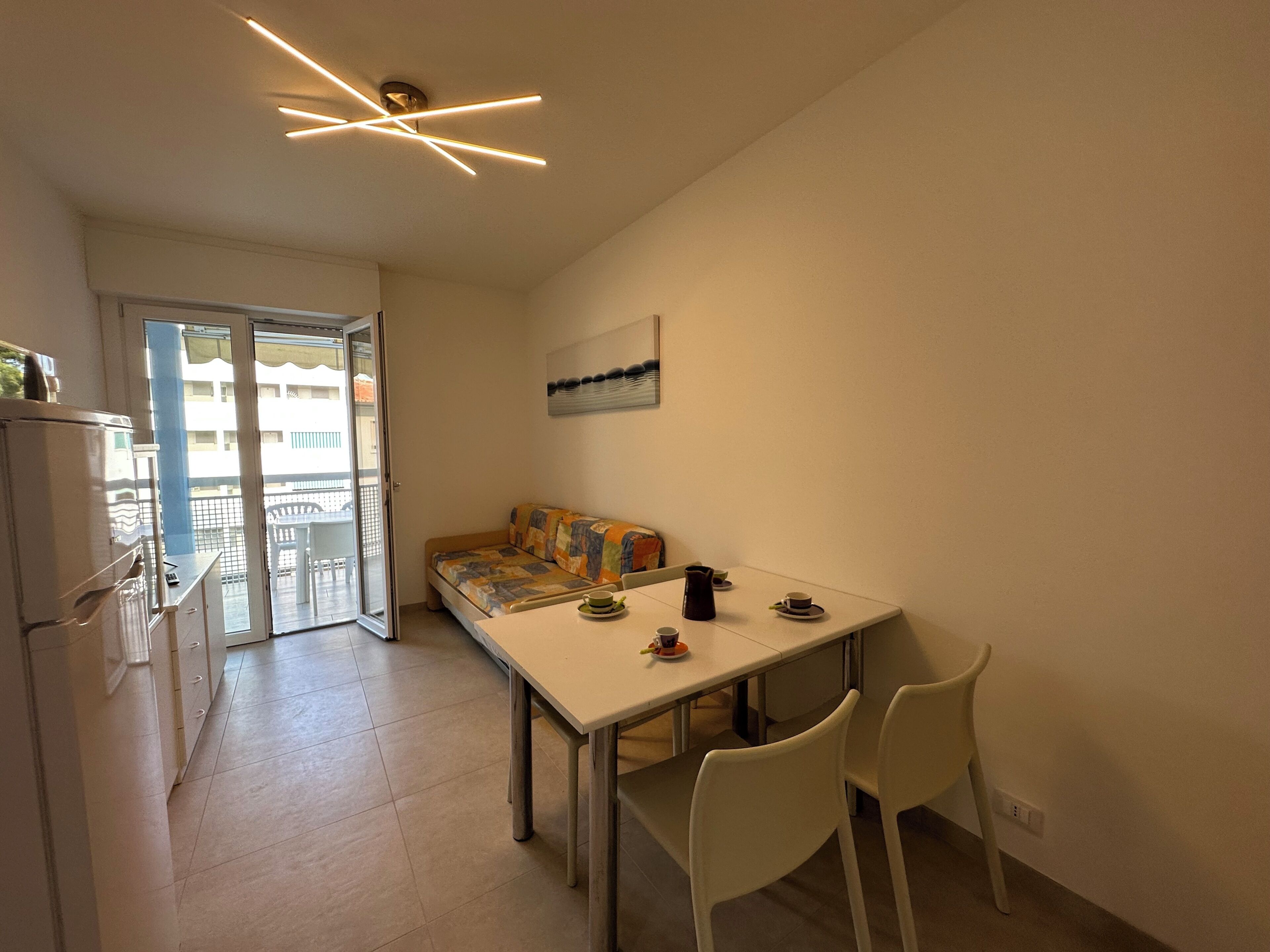 Un espacio habitable compacto con kitchenette, una mesa de comedor con sillas, un sofá y un balcón con vistas a los edificios.
