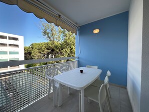 Ein Balkon mit weißem Tisch und Stühlen, Blick auf Bäume und Gebäude sowie eine blaue Wand.