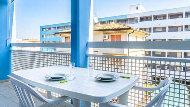 Un balcon avec une table et des chaises blanches, donnant sur un quartier résidentiel avec des immeubles.
