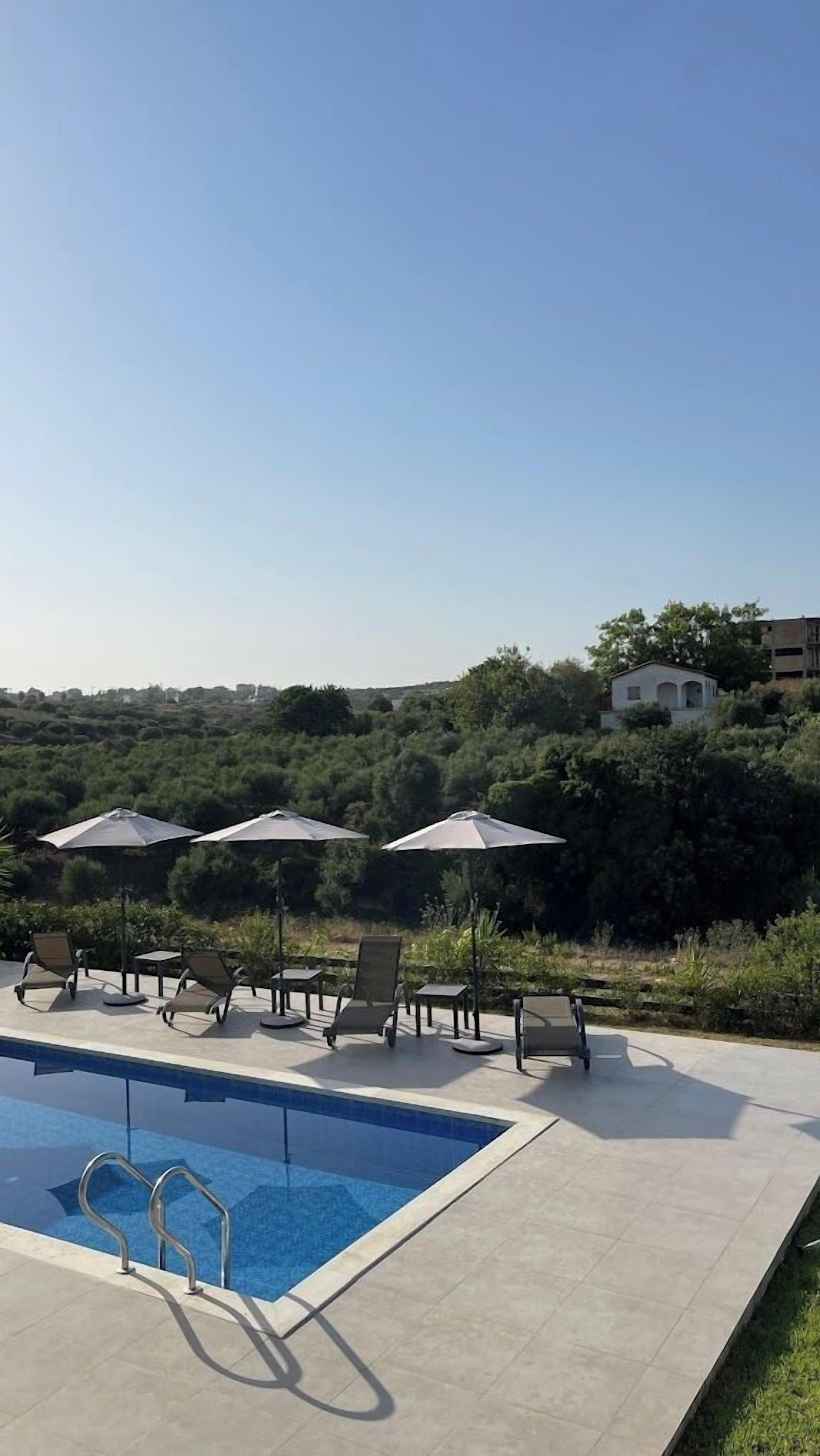A swimming pool with lounge chairs and umbrellas, surrounded by greenery and buildings in the background.