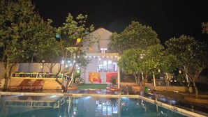 Ein Hotel bei Nacht mit Schwimmbad, gut beleuchtetes Gebäude und umliegender Bäume.
