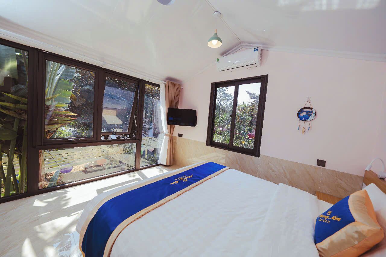 A hotel room with a large bed, a TV mounted on the wall, and a view of the outdoors through large windows.