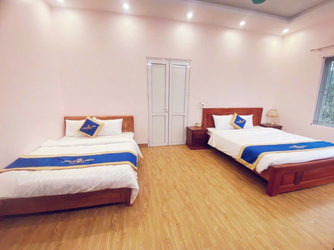 A hotel room with two beds, wooden flooring, a wardrobe, and a window.