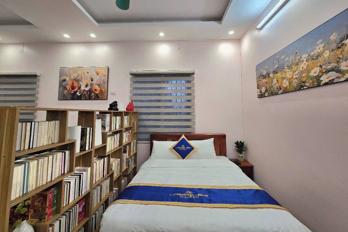 Een keurig opgemaakt slaapkamer met een bed, een boekenkast, een schilderij en een raam met jaloezieën.