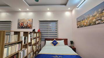 Een keurig opgemaakt slaapkamer met een bed, een boekenkast, een schilderij en een raam met jaloezieën.