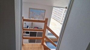 Eine schmale Treppe führt zu einem Schlafzimmer mit Dachfenster, Holzgeländern und Blick ins Freie.