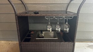 A wicker bar cart with three wine glasses and a bottle. - Redrocks Hot Tub Landing Pad (Littleton)