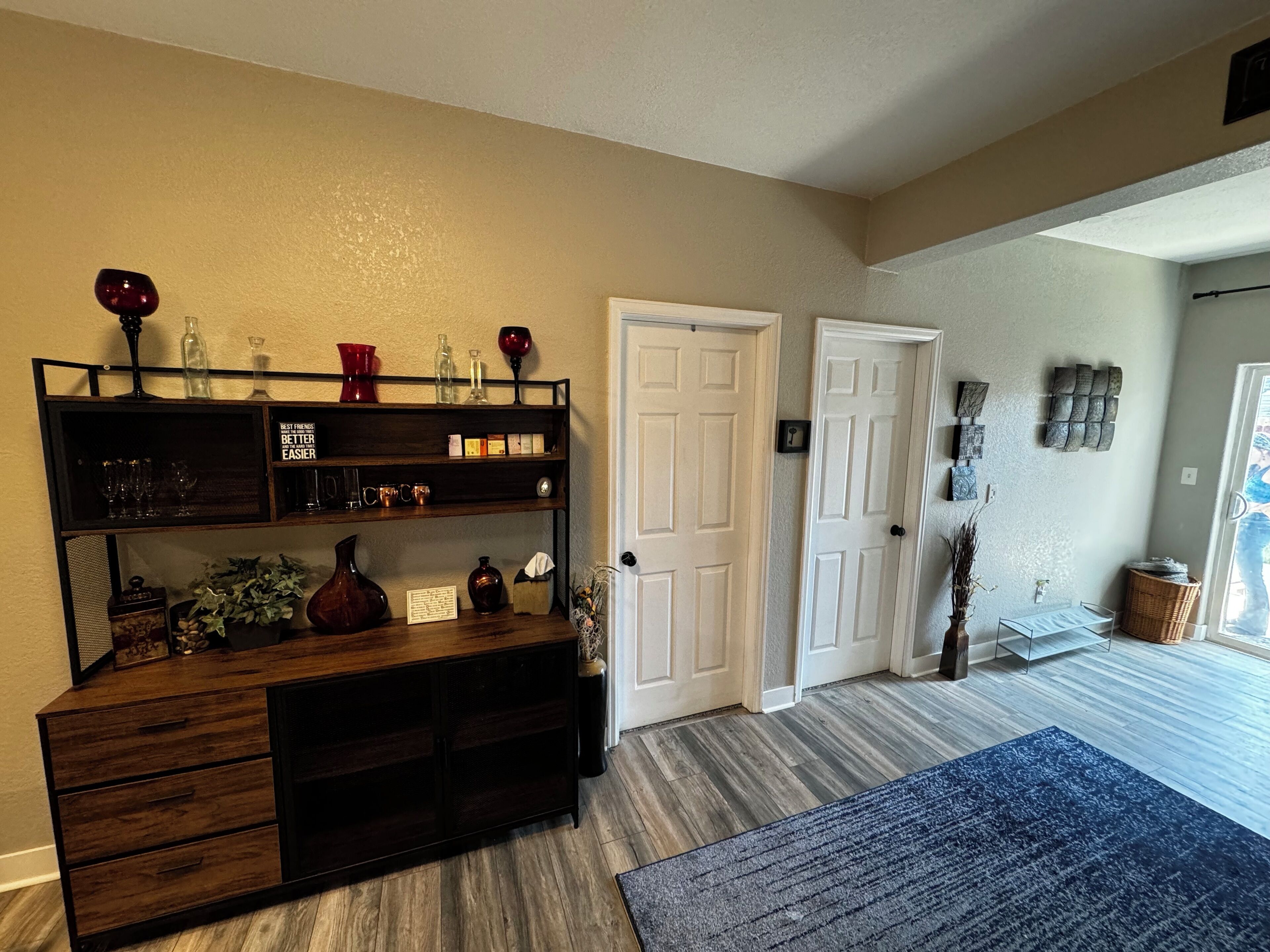 Quarto com mesa de consola de madeira, tapete azul e porta com interruptor de luz.