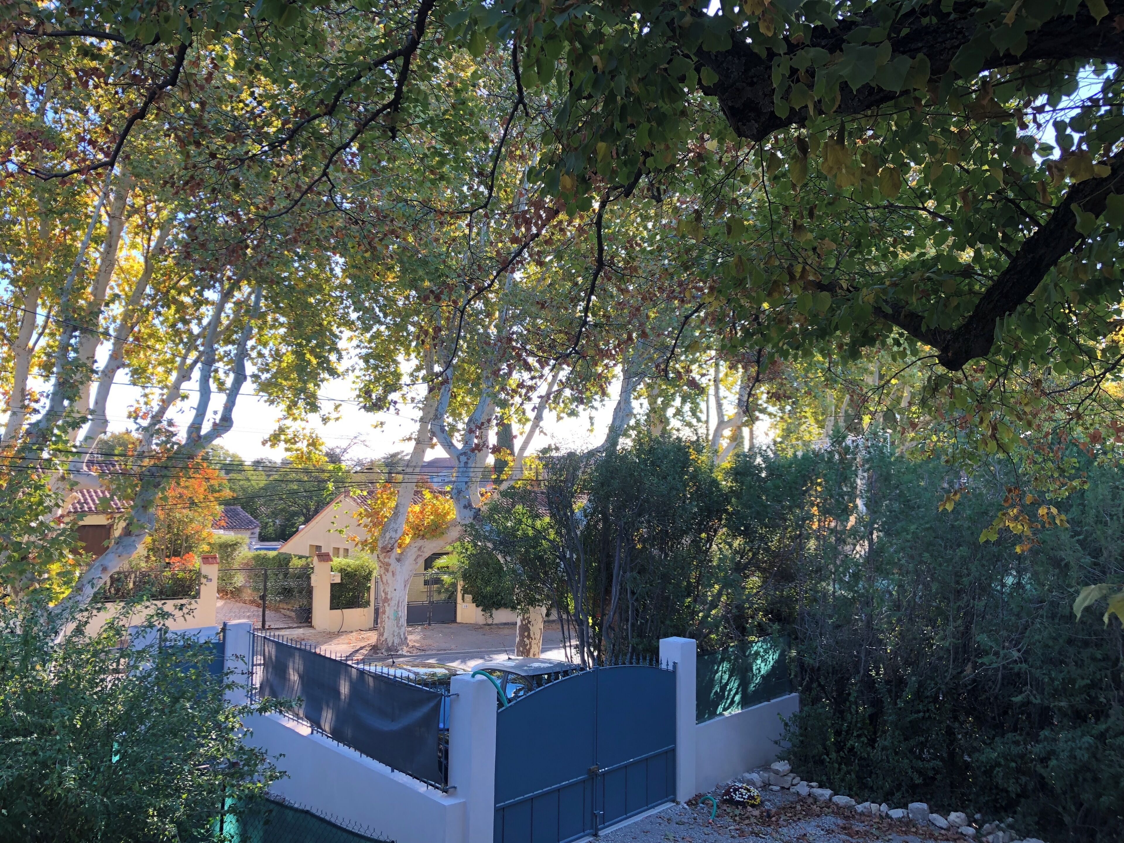 A residential area with a gated entrance, trees, and a building with a tiled roof.