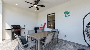 A patio area with a table and chairs, a ceiling fan, a grill, and a window. - Spacious 3-bedroom house in pleasant Cape Coral with AC and gym (Cape Coral)
