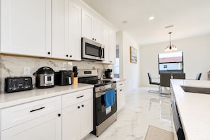 A modern kitchen with white cabinetry, a built-in microwave, a stove, and a toaster. - Spacious 3-bedroom house in pleasant Cape Coral with AC and gym (Cape Coral)