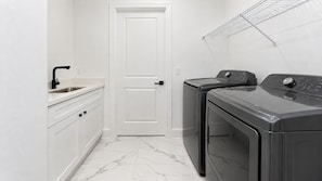 A laundry room with a washing machine, a dryer, and a sink. - Spacious 3-bedroom house in pleasant Cape Coral with AC and gym (Cape Coral)