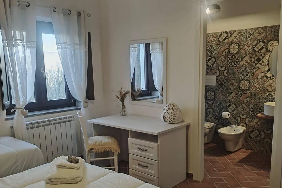 A bedroom with two beds, a desk, a mirror, and a bathroom with a patterned wall.