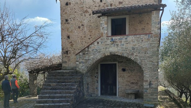 A rustic stone building with a tiled roof, a central arched doorway, and a staircase leading to the entrance. - Agriturismo Li Guira (Stio)