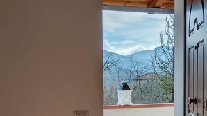 A room with a bed, a bedside table with a lamp, a wooden ceiling, and a view of mountains through an open door. - Agriturismo Li Guira (Stio)