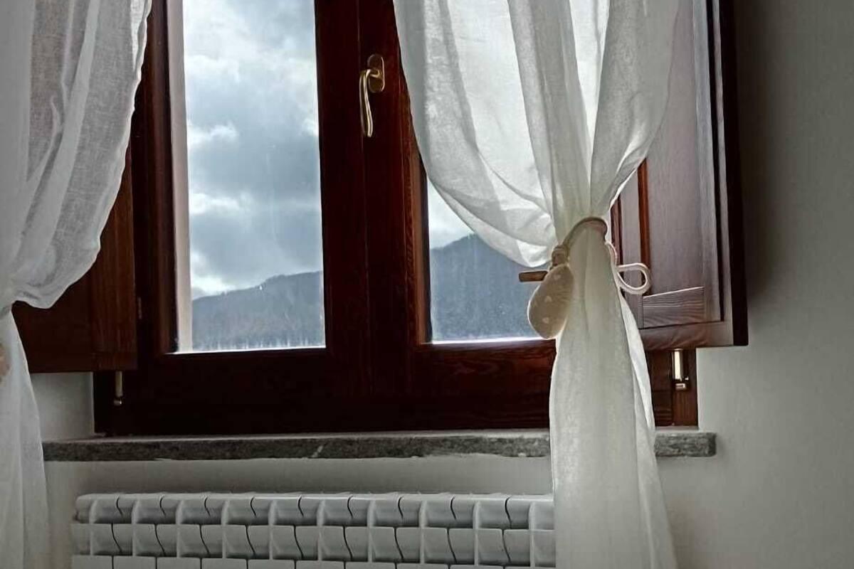A bedroom with a bed, a window with curtains, a radiator, and a tray with towels and stones.