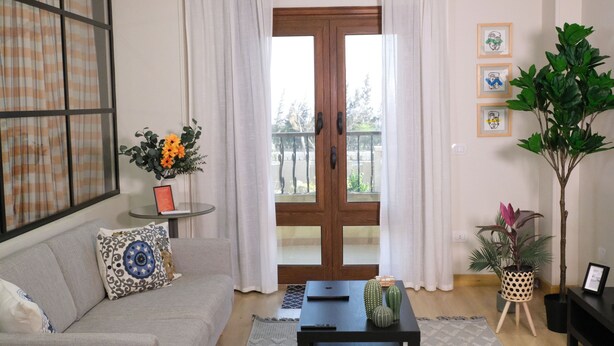 Ein Wohnzimmer mit einer Couch, einem Couchtisch, einer Topfpflanze und einer Glastür, die auf einen Balkon führt.