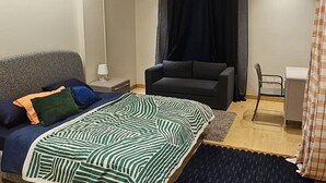 Ein Schlafzimmer mit Bett, Stuhl, Schreibtisch und einem Fenster mit Vorhängen.