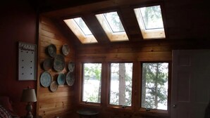 Una habitación acogedora con paredes de madera, una cama, una lámpara, un esparacero de pared y tragaluces.