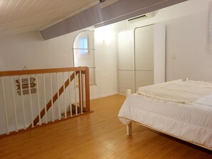Een slaapkamer met een houten vloer, een wit bed, een witte balustrade en een kast met schuifdeuren.