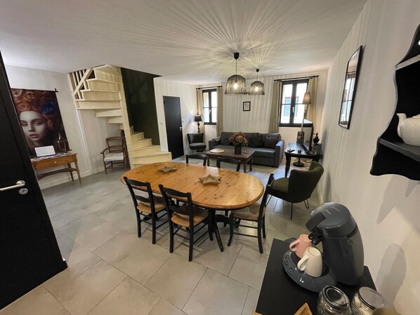 A modern living room with a dining area, featuring a staircase, a sofa, a coffee table, and a coffee machine. - Welcome to Le Trois Six Very nice air-conditioned duplex (Pézenas)