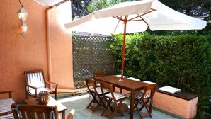 A patio with a wooden table and chairs, a white umbrella, and a wicker chair.