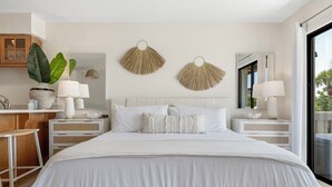 A modern bedroom with a large bed, two bedside tables with lamps, a large mirror, and a view of the outdoors. - The Mini Pearl 30A beach studio - Dog Friendly! (Santa Rosa Beach)