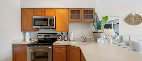 A modern kitchen with wooden cabinets, stainless steel appliances, a large island, and a hanging plant.