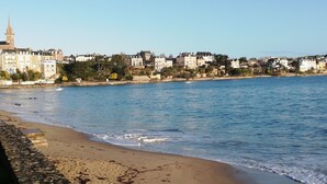Eine Küstenstadtlandschaft mit Sandstrand, ruhiger See und verschiedenen Gebäuden, darunter ein markanter Turm.