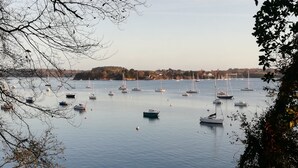 Ein Yachthafen mit mehreren Booten, die in ruhigem Wasser vor Anker liegen, umgeben von Bäumen und einer entfernten Küstenlinie.