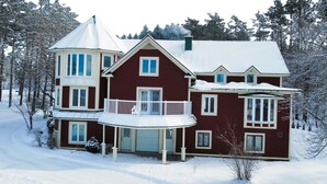 A large, two-story house with a balcony, surrounded by snow-covered trees.