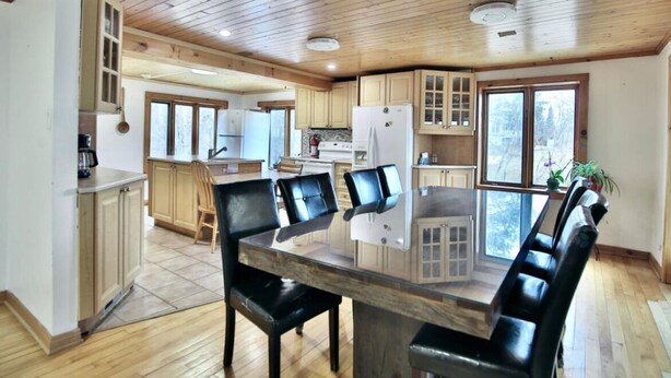 A spacious kitchen with wooden cabinets, a central island, and a dining area with a glass table and black chairs.