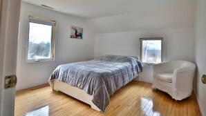 A bedroom with a bed, a chair, and two windows.