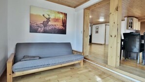 A wooden-floored room with a grey sofa, a wooden ceiling, and a painting of a deer on the wall.