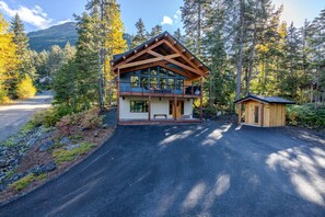 A two-story log cabin with a balcony, surrounded by a forest and a mountain in the background. - 3 King Suites Near Alyeska | Sauna & Mountain Views (Girdwood)