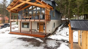 A two-story log cabin with a balcony, large windows, and a wooden deck. - 3 King Suites Near Alyeska | Sauna & Mountain Views (Girdwood)