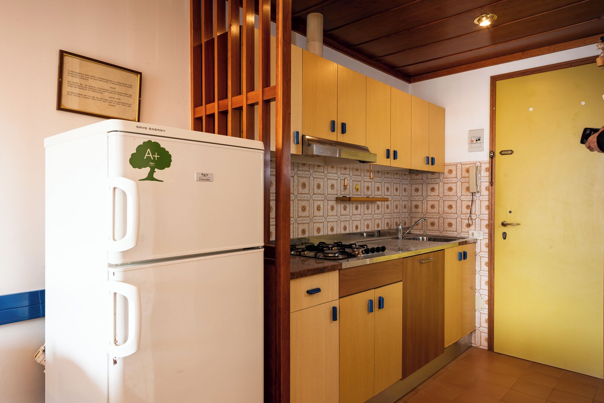 A compact kitchen with wooden cabinets, a white refrigerator, a gas stove, and a yellow door.