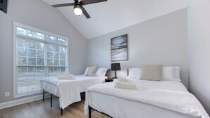 A bedroom with two beds, a ceiling fan, a window with blinds, and a painting on the wall.