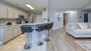 A modern kitchen with bar stools, a dining area with a sofa, and a living room with a coffee table.