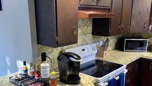 A kitchen with dark wood cabinets, a white stove, a microwave, and a coffee maker on a marble countertop. - Charming 3-bedroom house with WiFi, AC in serene Towamensing Trails (Towamensing Trails)
