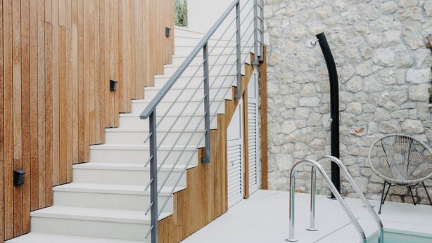 Ein moderner Poolbereich im Freien mit einer Holztreppe und einer Steinmauer.